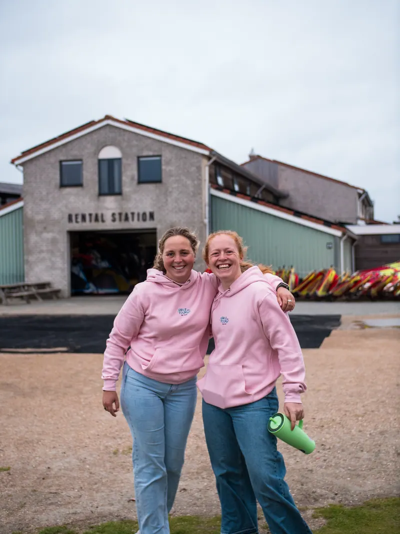 Two Girls on Tour riders in the crew hoodie outside a windsurf rental station